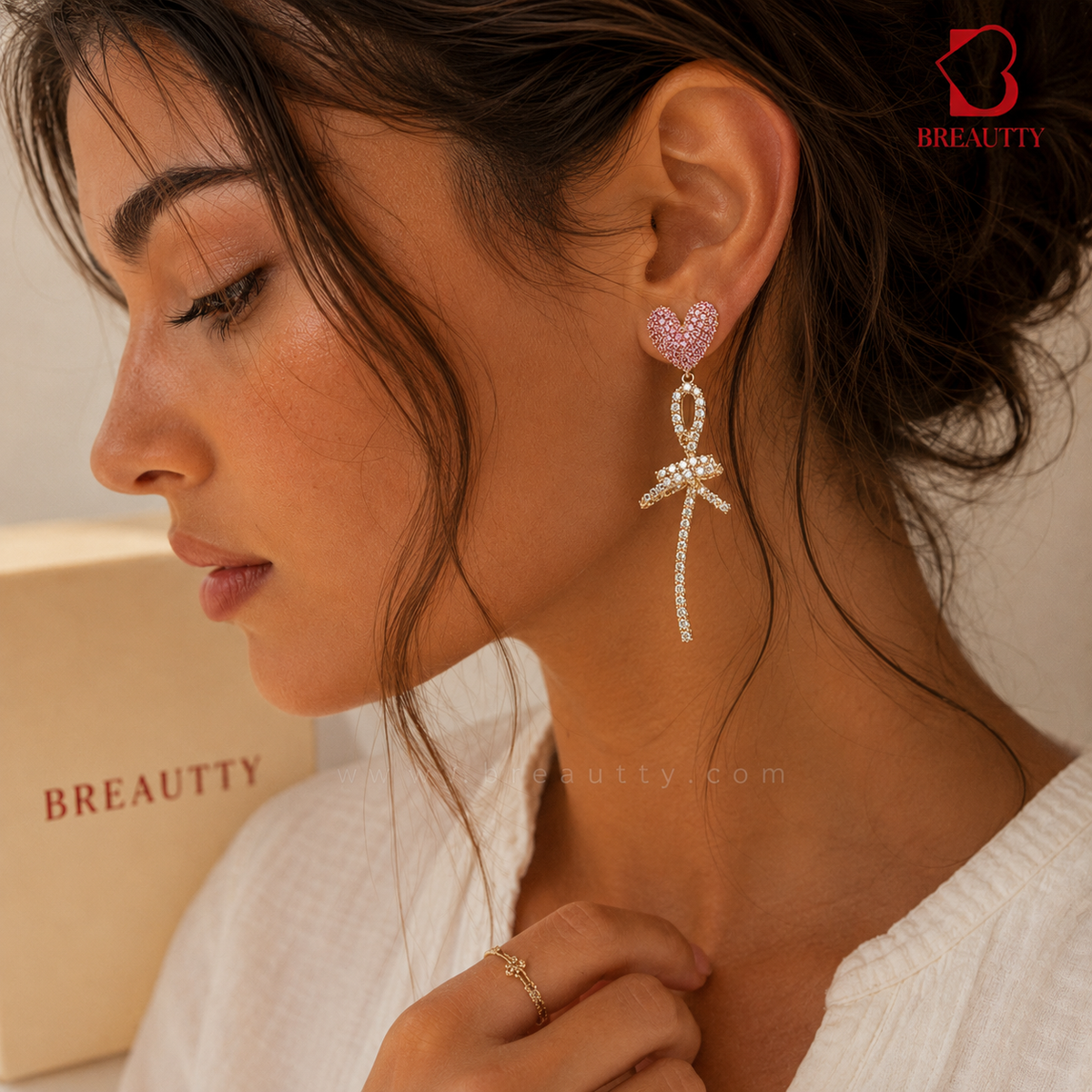Woman wearing a bow-shaped earring with a pink heart charm, with 'BREATUTY' branding in the background.
